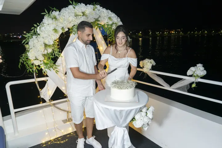 Çiçek takı önünde nişan pastası kesen çift, yatta nişan ve söz